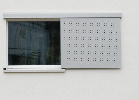 Fenster mit Schiebeladen als Sonnen- und Einsichtschutz ermöglichen den Verzicht auf wärmetechnisch ungünstige Hohlstürze. Die Schiebeladenkonstruktion ist über Spezialelemente «wärmebrückenfrei» in die tragende Wand befestigt.